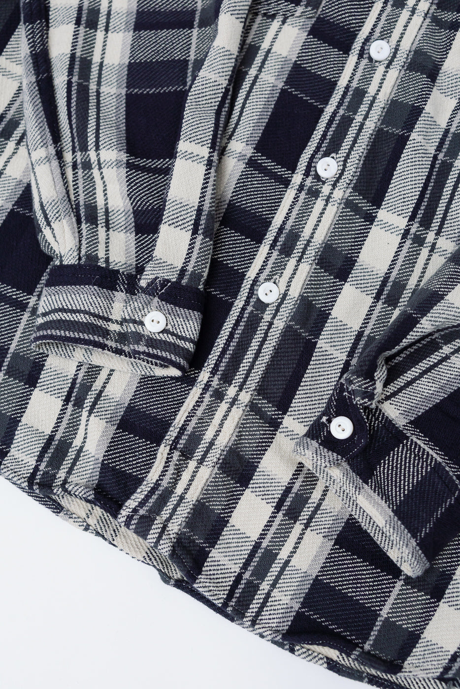 Close-up of front hem and cuffs of grey plaid cotton flannel shirt, showing white buttons and fabric texture.