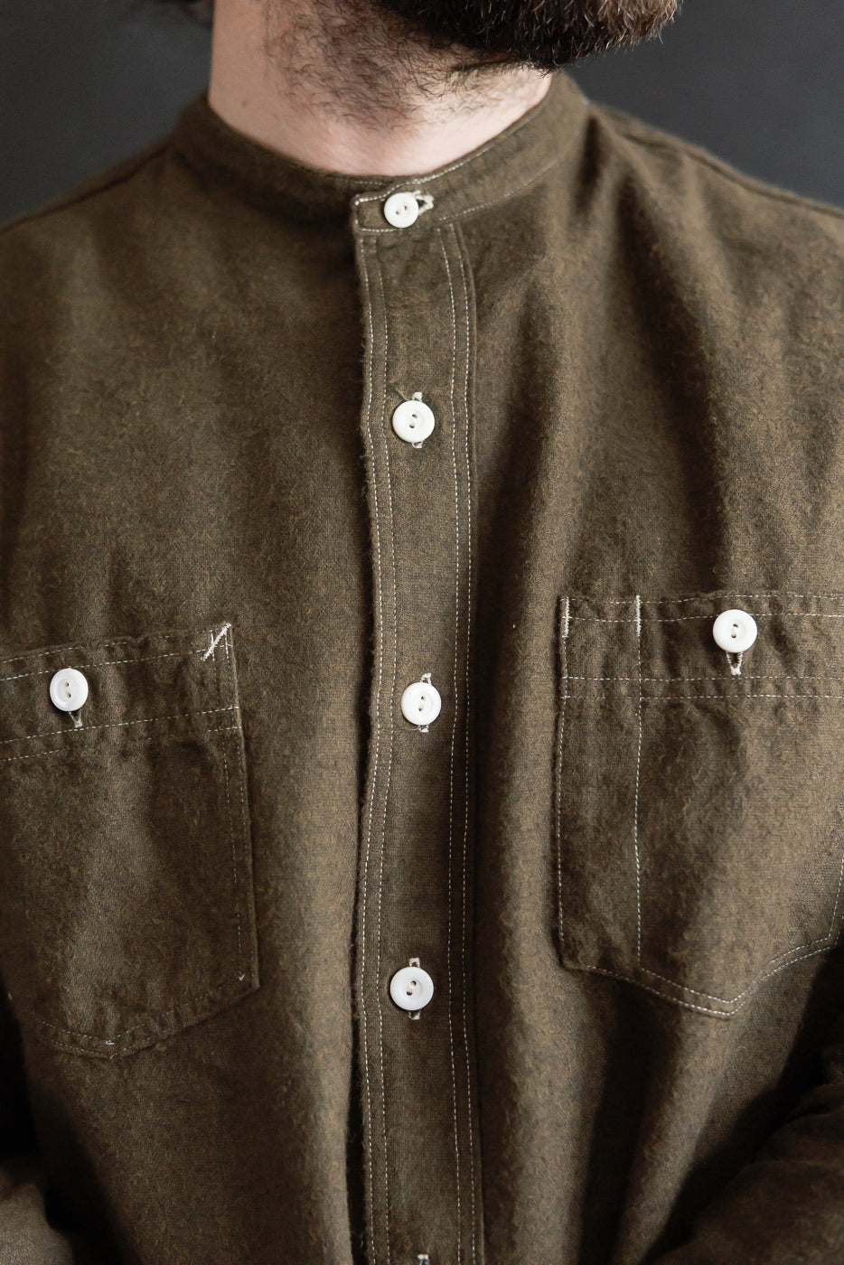 Close-up front of men's Post O’alls St. Louis Band cotton heather flannel shirt in tobacco, showing white buttons, two chest pockets, and band collar. Male model, 5'9