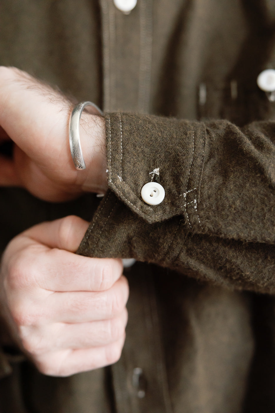 Close-up of male model adjusting cuff on olive heather flannel shirt sleeve, featuring button detail and fabric texture.