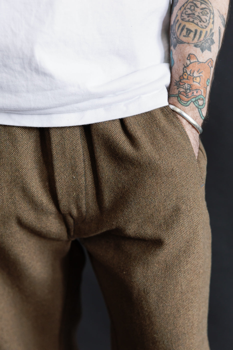 Close-up front view of brown basket tweed pants on male model, 5'9, 165lbs, athletic build, showing fabric texture and pleated waistband.
