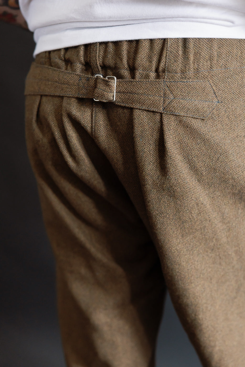 Close-up back view of Post O'Alls brown basket tweed pants on male model, showing back waist cinch detail, athletic build, part of Dant contemporary casual apparel collection.