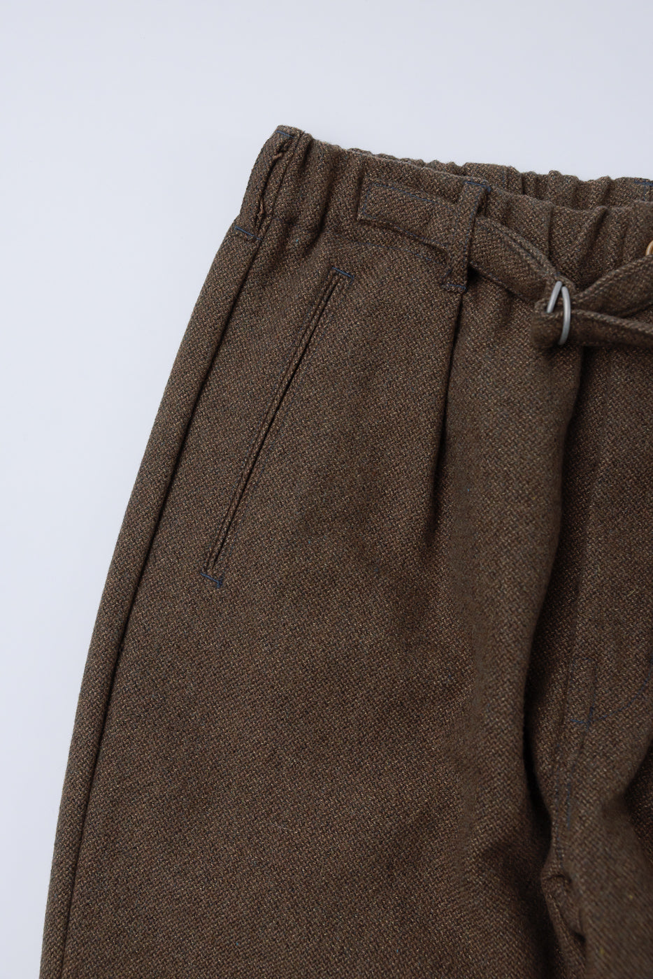 Close-up front view of brown basket tweed pants showing waistband, belt loop, and pocket detail