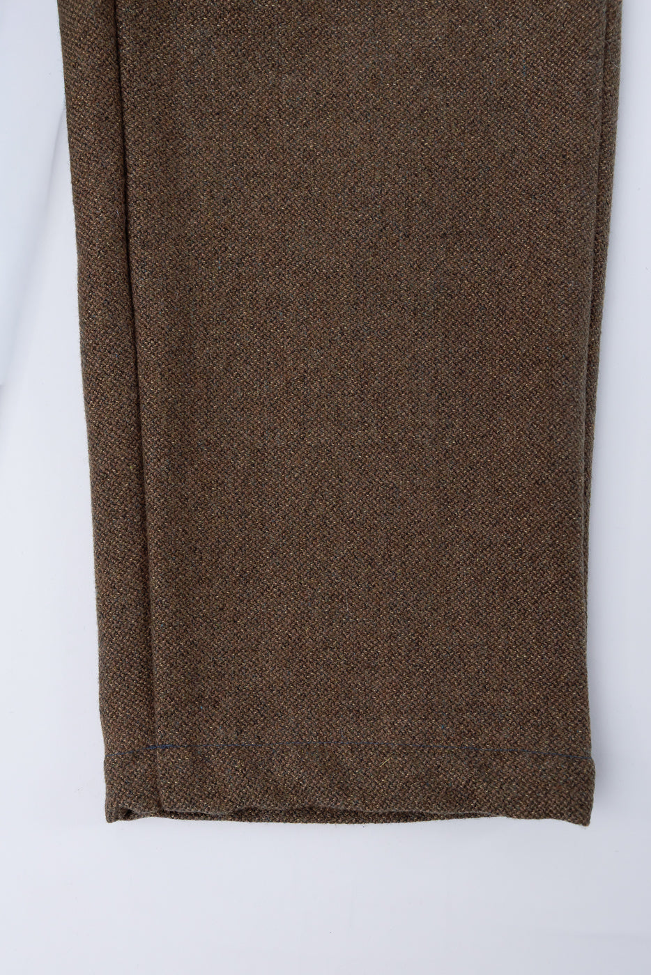 Close-up of front lower leg and hem on brown basket tweed pants, showing fabric texture.
