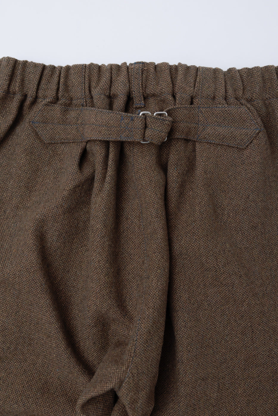 Close-up of back waistband and adjustable strap on brown tweed pants, fabric texture visible