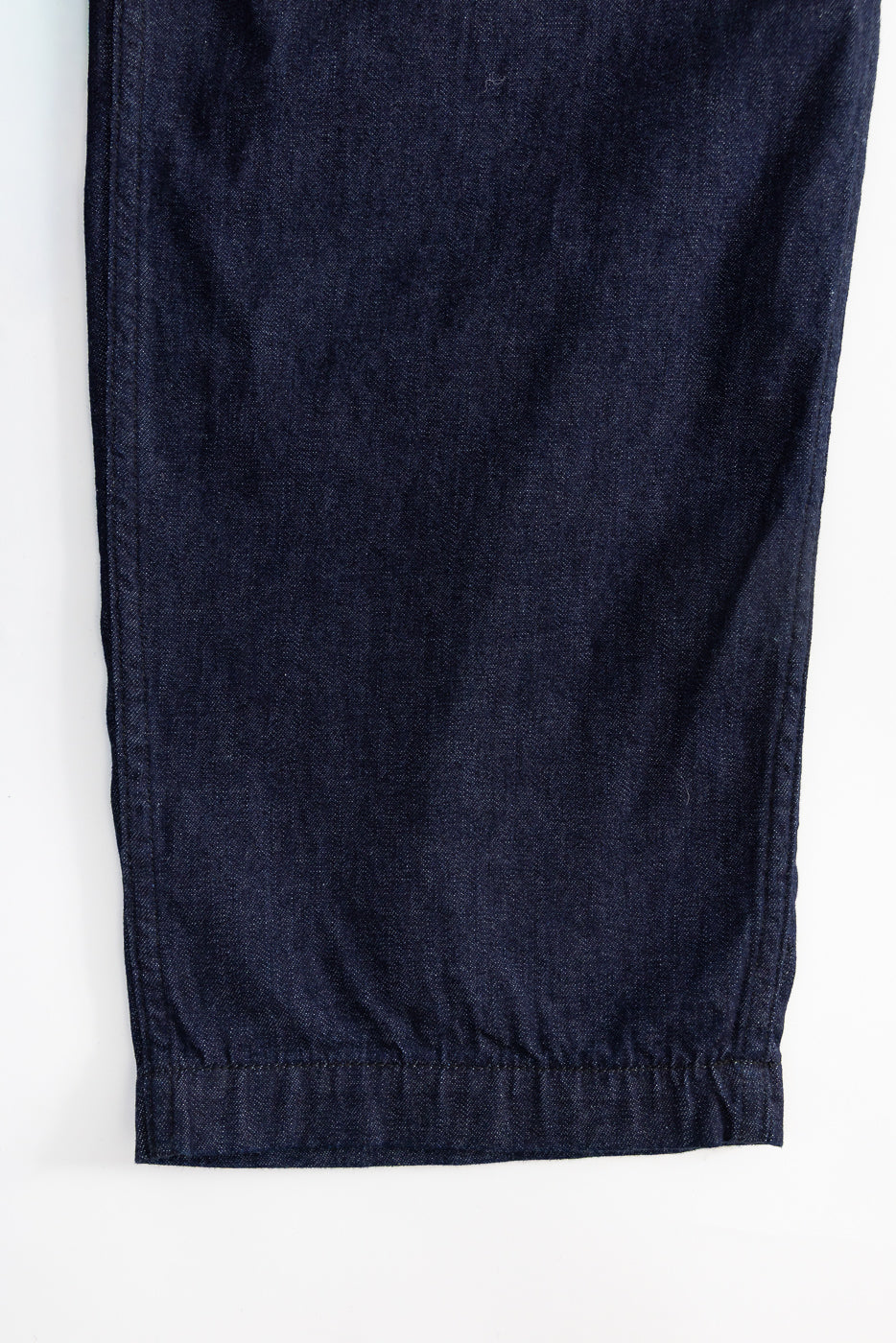 Close-up of dark indigo denim pants, showing front lower leg and hem detail.