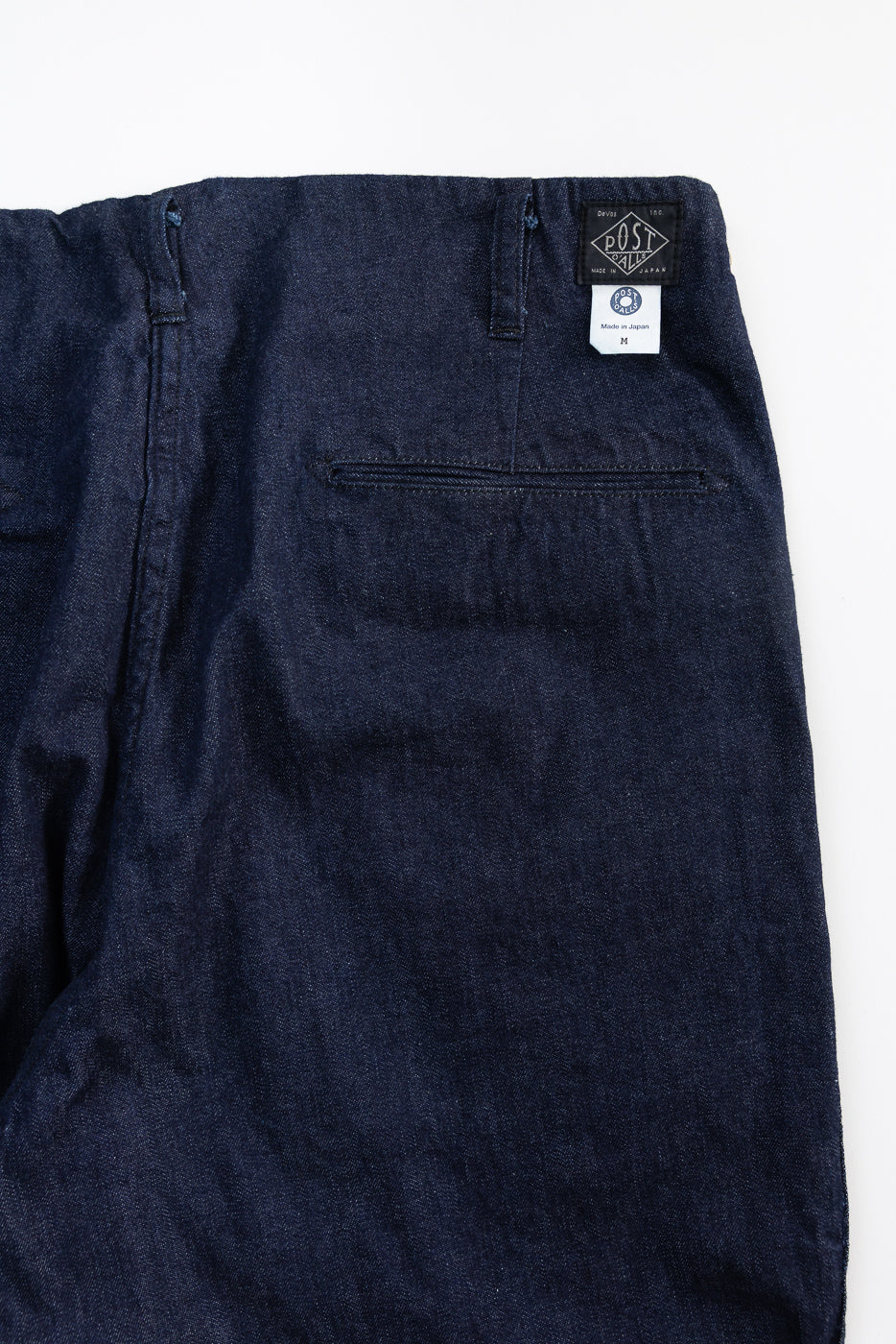 Close-up of back side of dark indigo denim pants showing pocket, belt loops, and tags