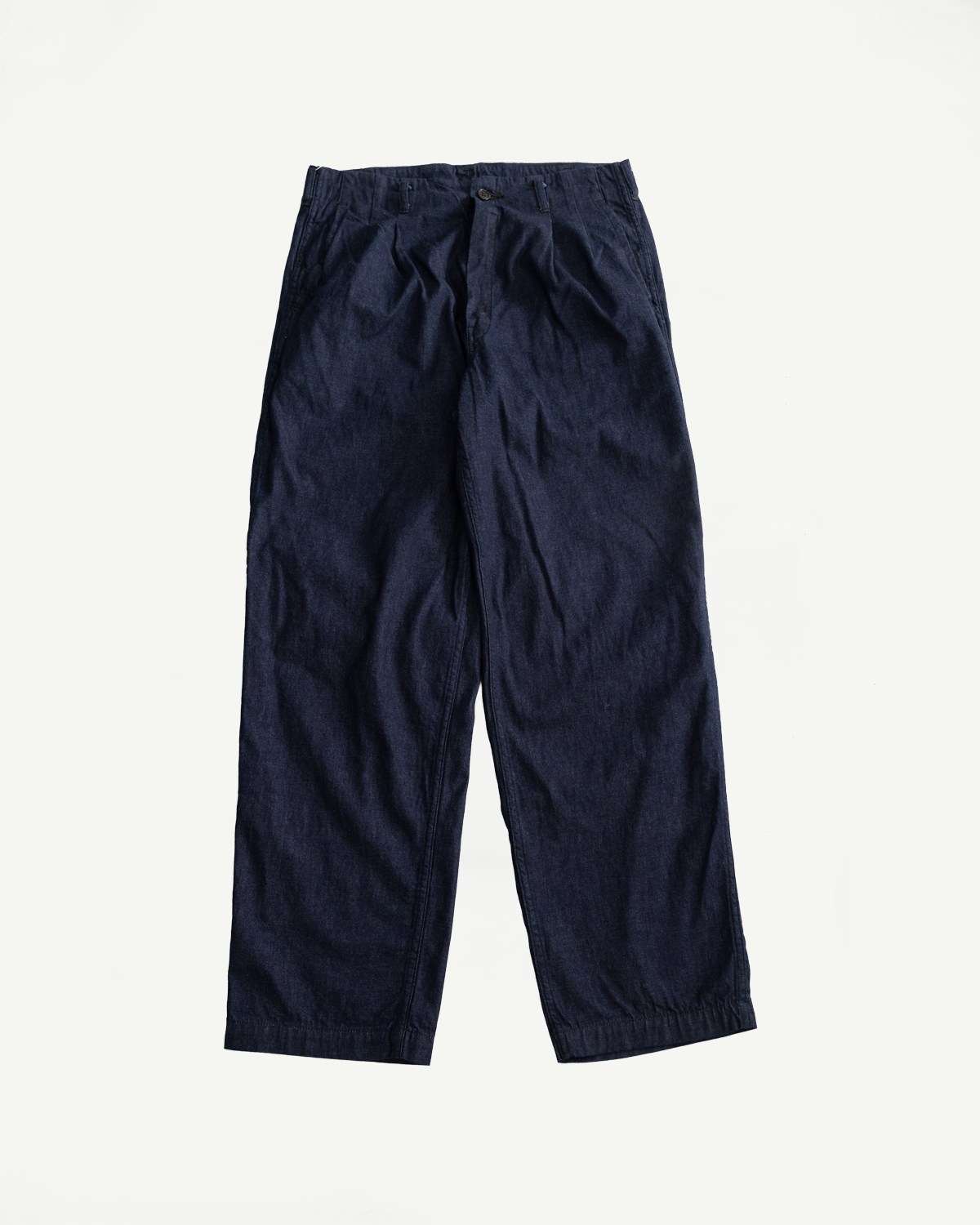 Flat lay, front view of dark indigo denim pants with pleated waist and button closure.