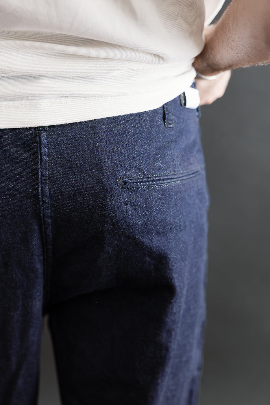 Close-up of back side of dark indigo denim pants on male model, showing rear pocket detail.
