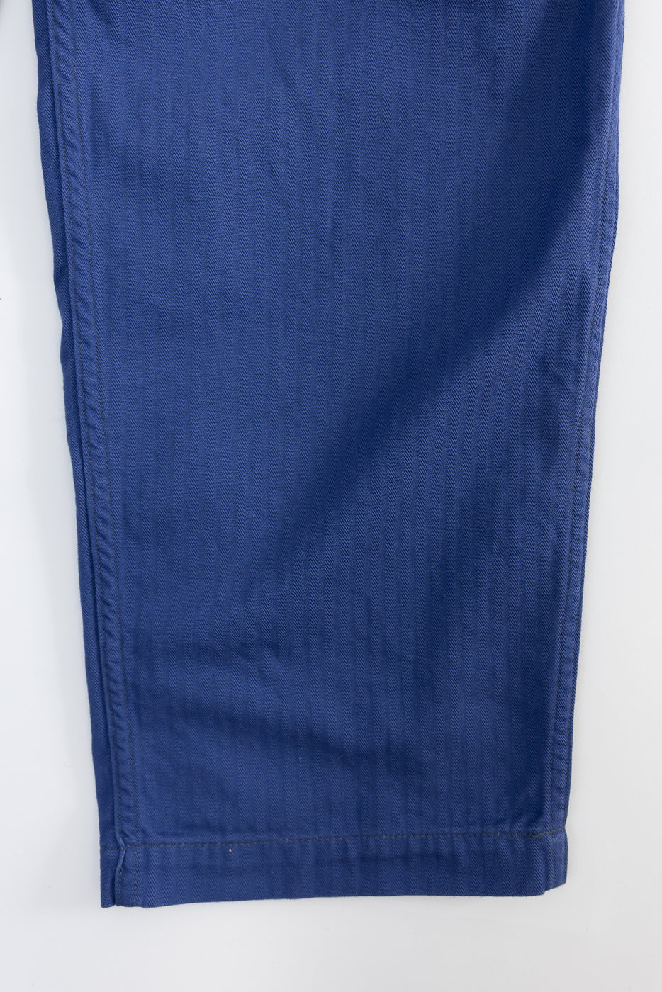 Close-up of blue herringbone twill pants hem, showing fabric texture and stitching detail, front leg view.