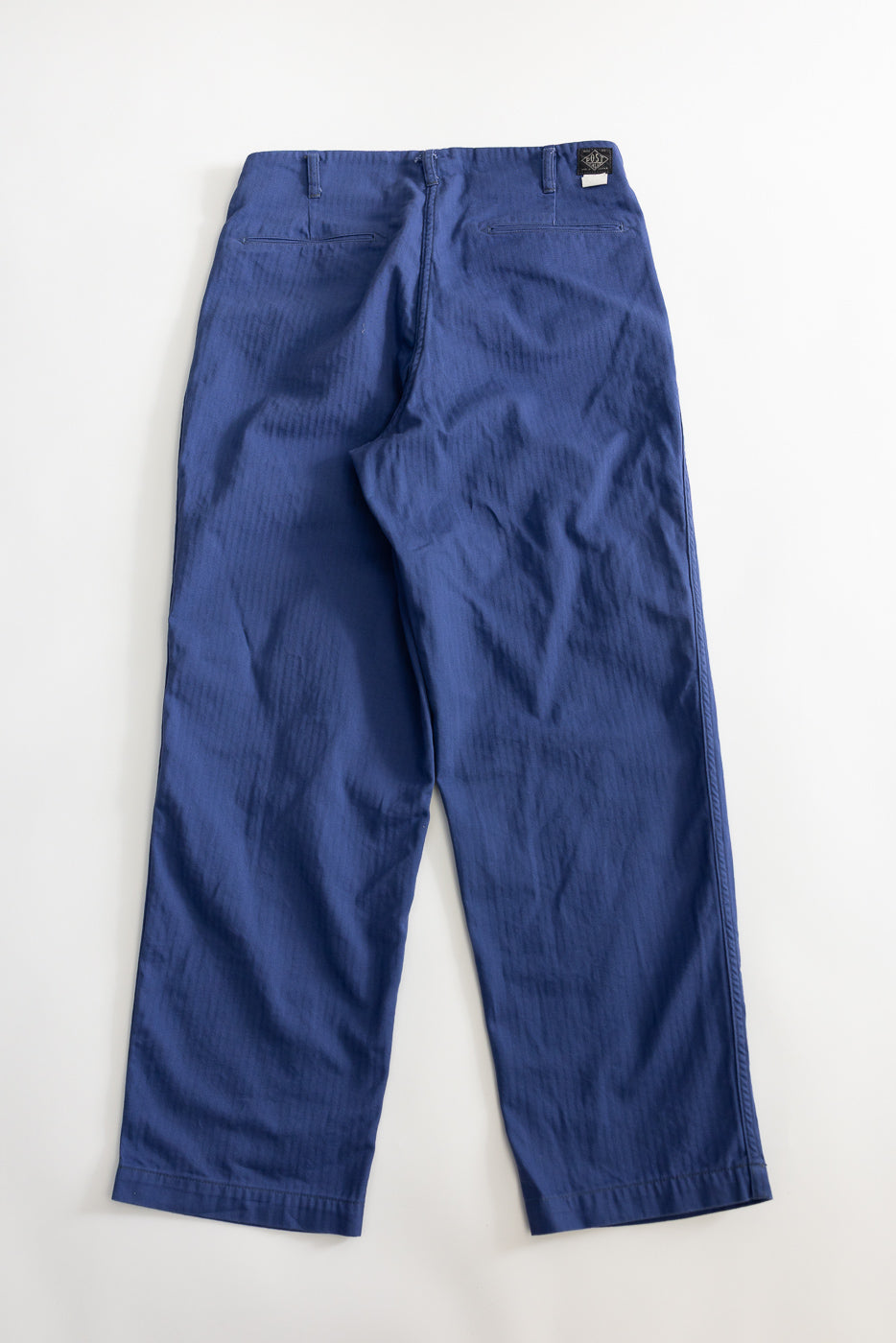 Flat lay of blue mini herringbone twill pants, back side, showing rear pockets and waistband tag