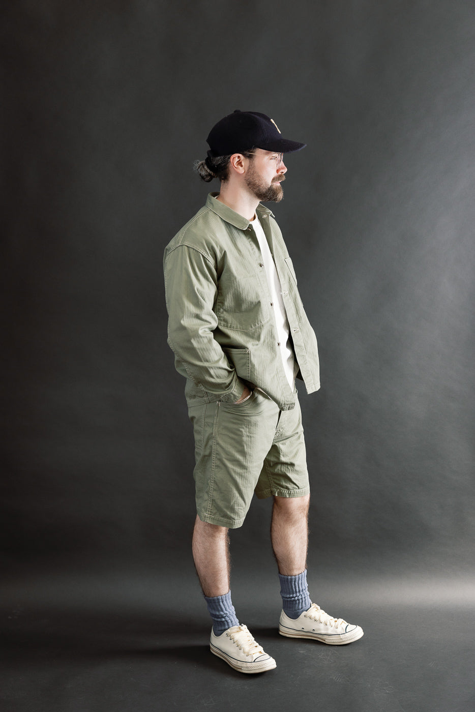 Full body side view of male model 5'9 165lbs athletic build wearing sage green jacket and shorts set in herringbone fabric.