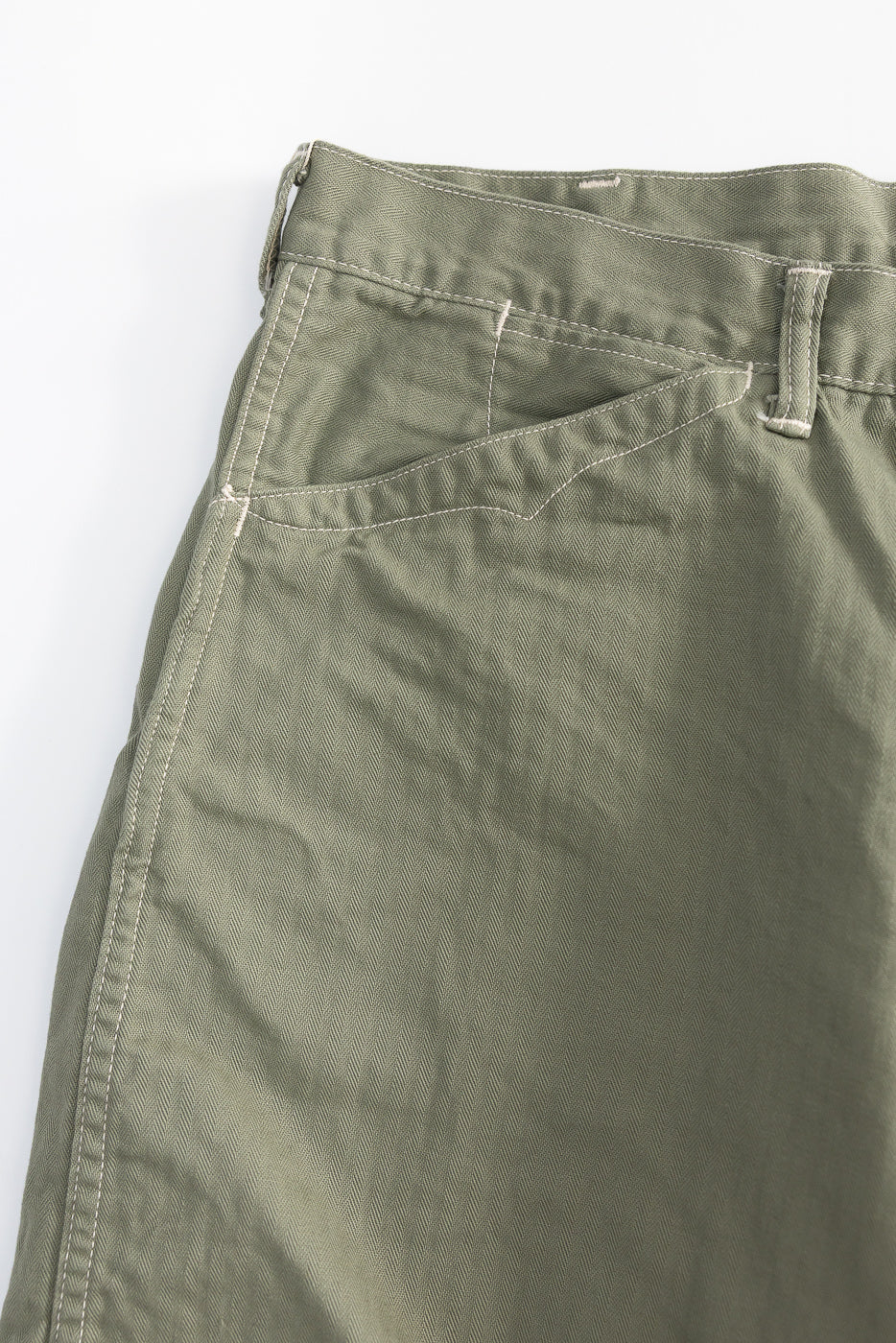 Close-up of front left side of sage green herringbone shorts, showing pocket and waistband stitching detail.