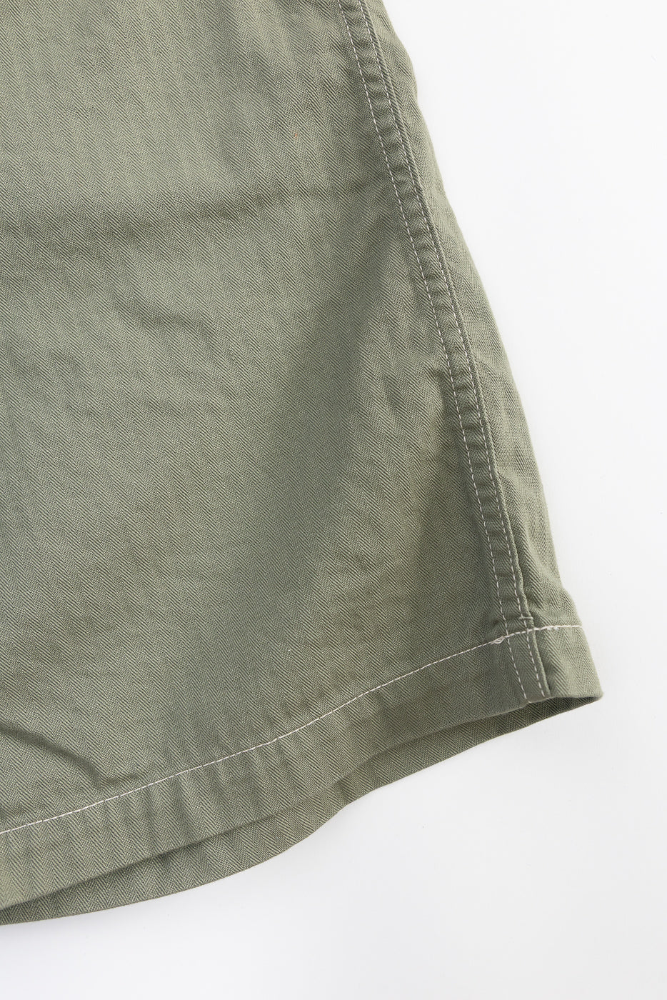 Close-up of sage herringbone twill shorts hem, showing fabric texture and stitching, front side.