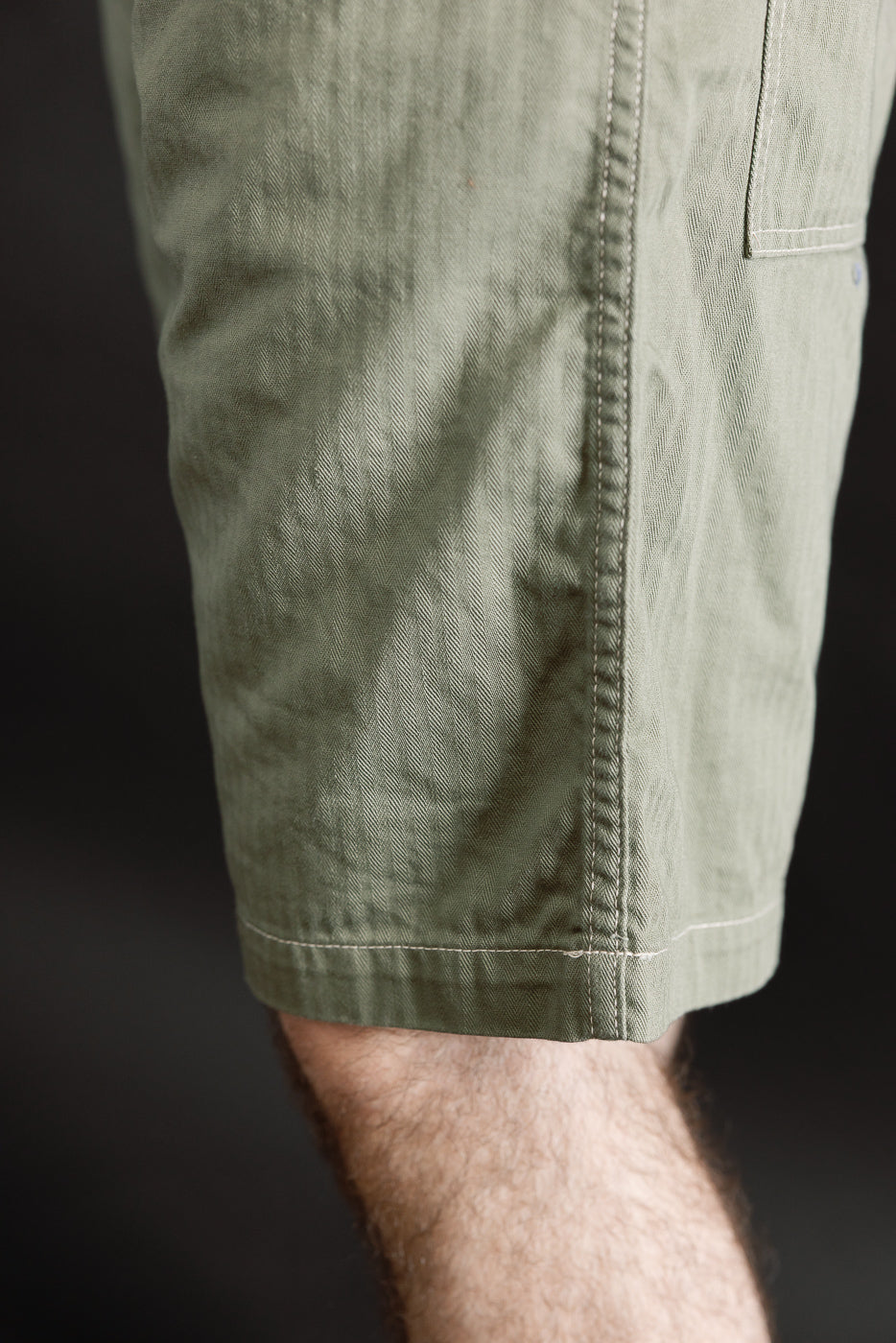 Close-up of men's sage green herringbone shorts, left side hem, model 5'9