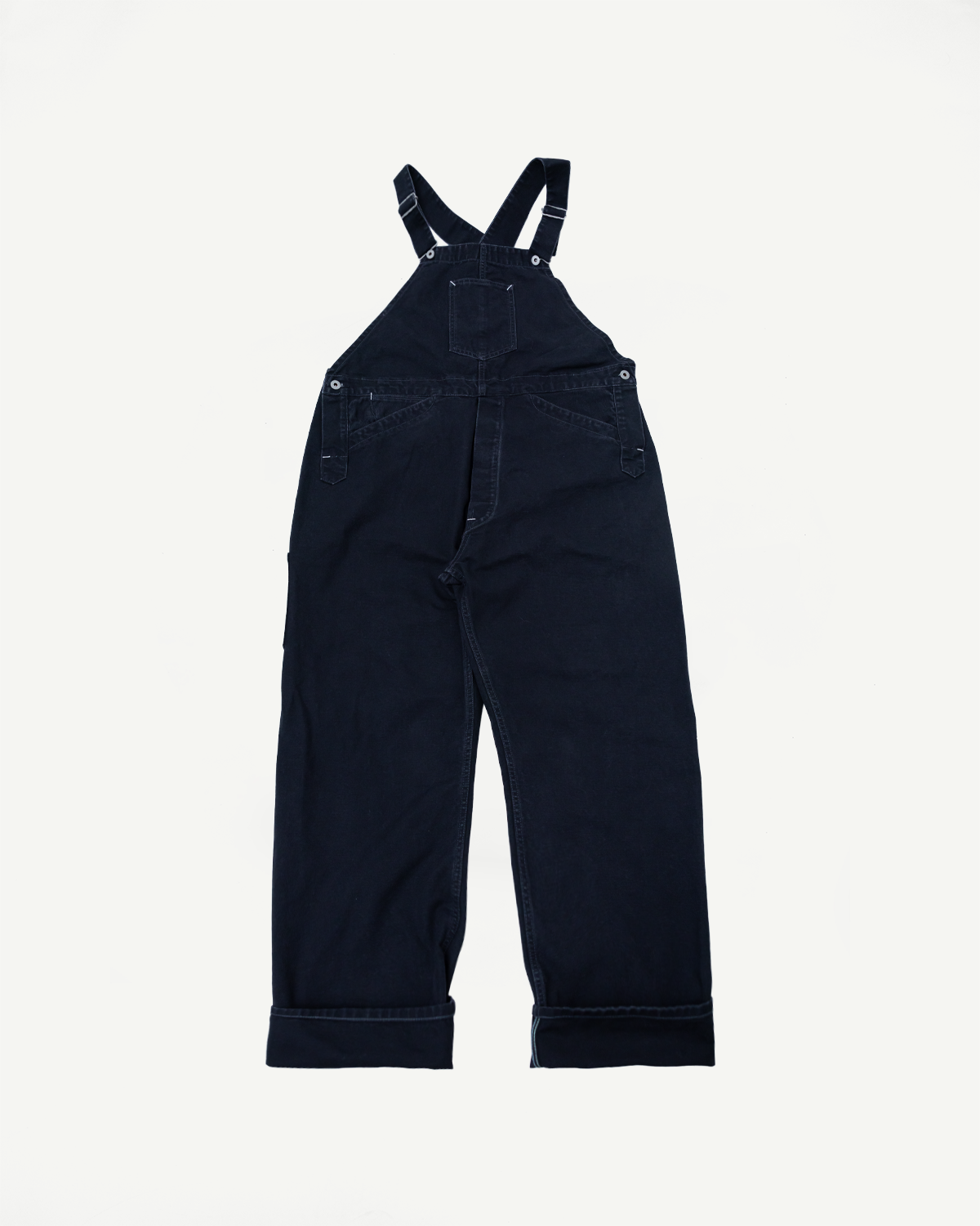 Flat lay back view of black pigment-dyed canvas overalls, showing pockets and straps