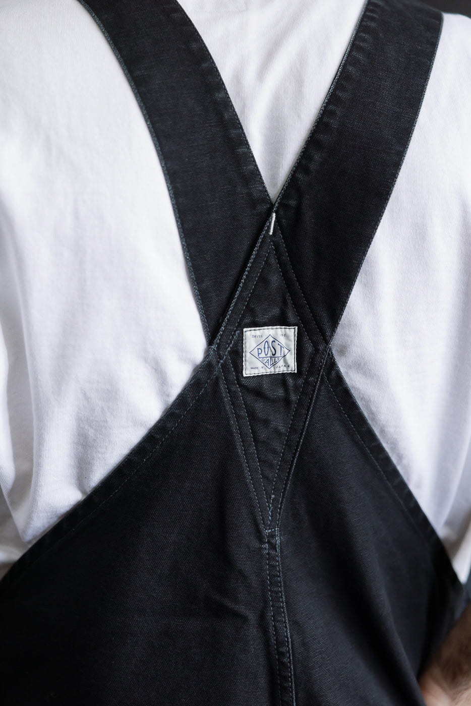 Close-up of back straps and tag on black pigment-dyed canvas Post Overalls, male model 5'9