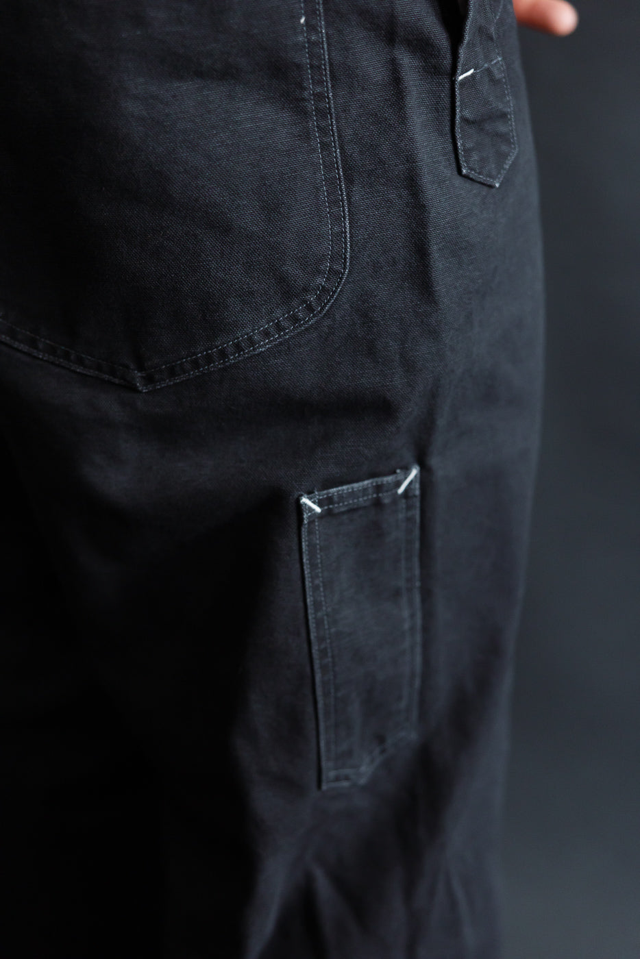 Close-up of black pigment-dyed canvas overalls, side view showing back pocket and stitching detail.