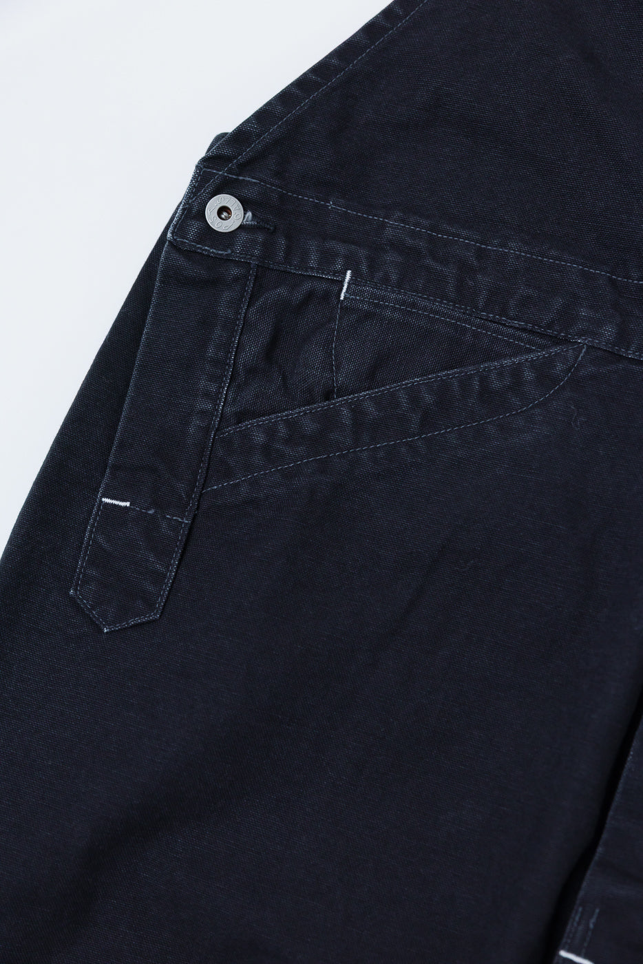 Close-up of black pigment dyed canvas overalls, side pocket and button detail, Dant.