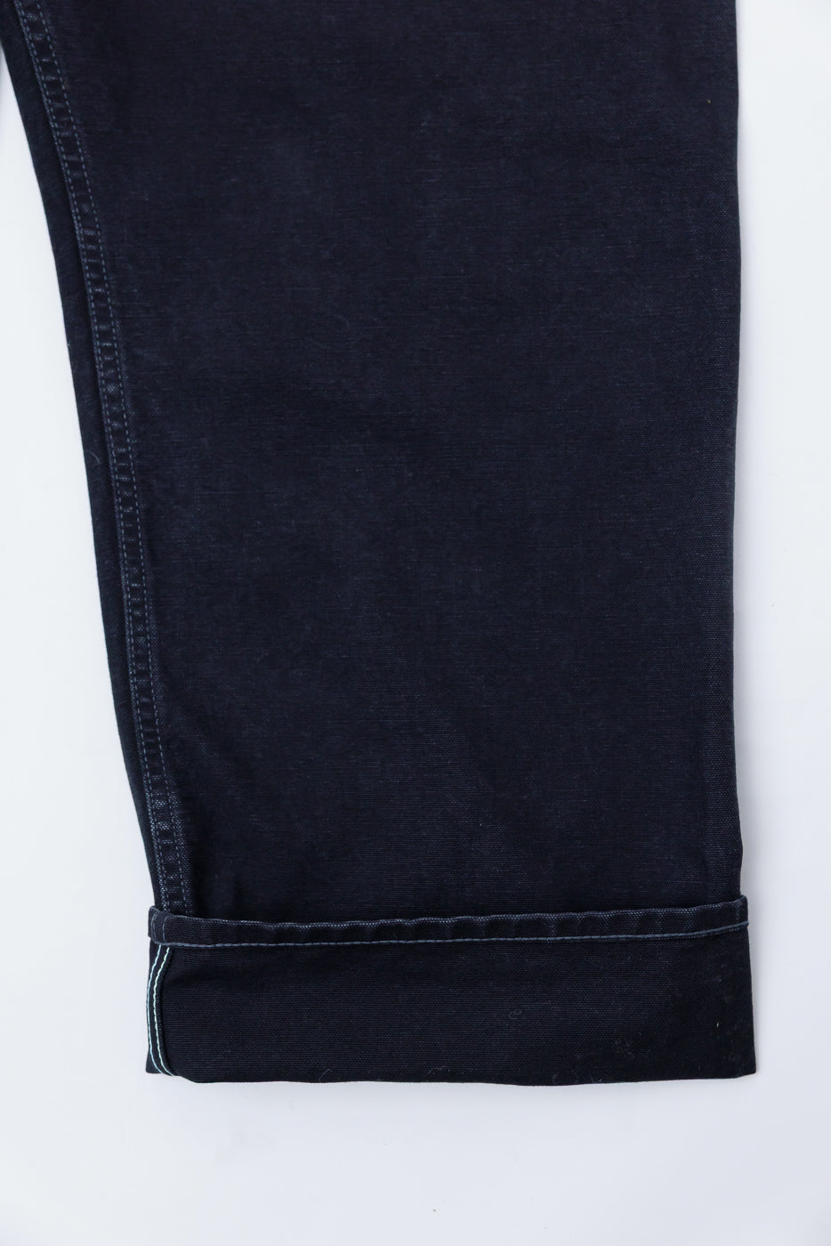 Close-up of black pigment-dyed canvas overalls leg, front side, showing cuff and stitching detail