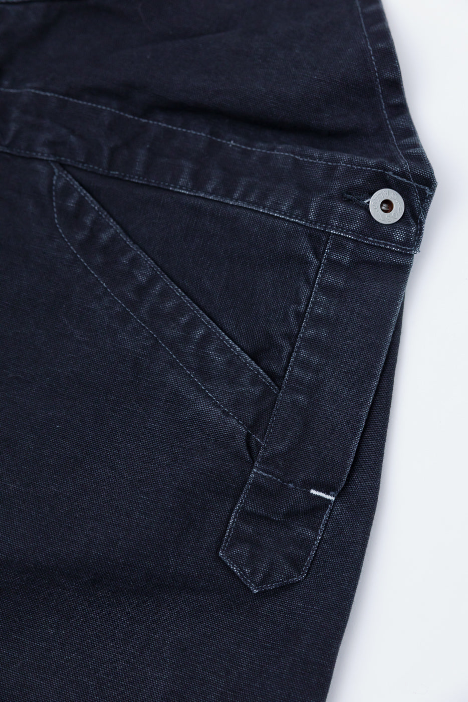 Close-up of Post O'Alls black pigment dyed canvas overalls, front left pocket stitching and metal button detail, contemporary casual workwear from Dant.
