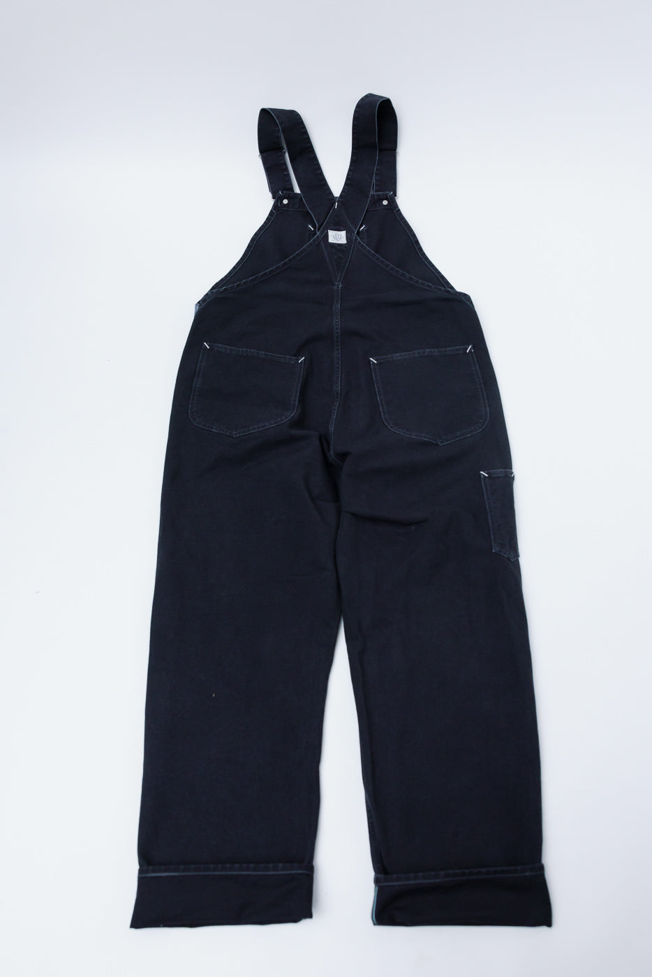 Flat lay, back view of Post O'alls black pigment dyed canvas overalls showing rear pockets and straps