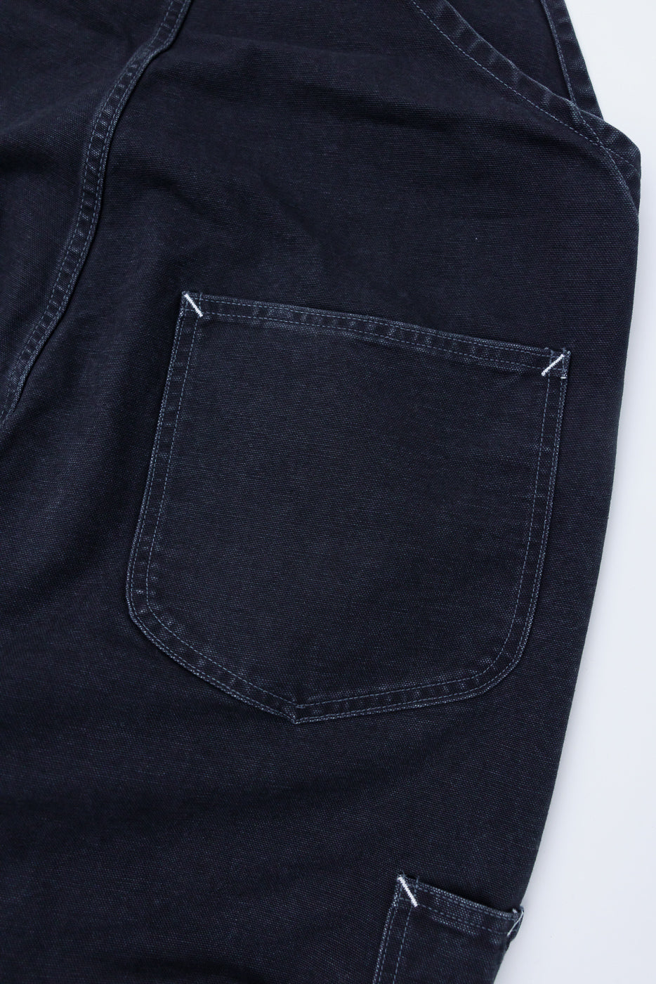 Close-up of back pocket and fabric texture on black pigment-dyed canvas overalls, back side.