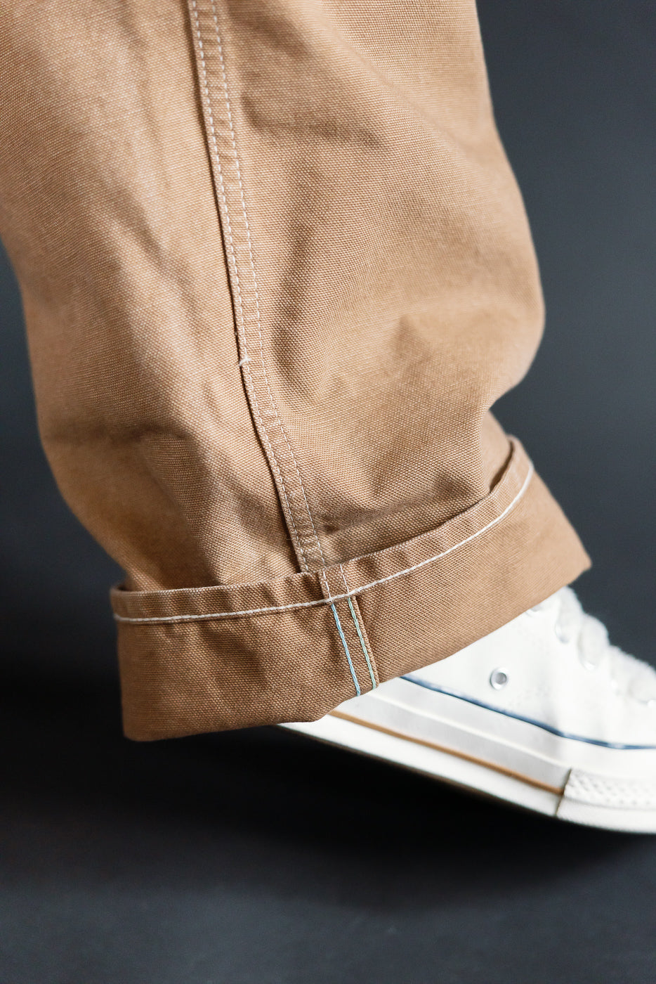 Close-up of hem and side seam on front right leg of washed brown pigment-dyed canvas overalls