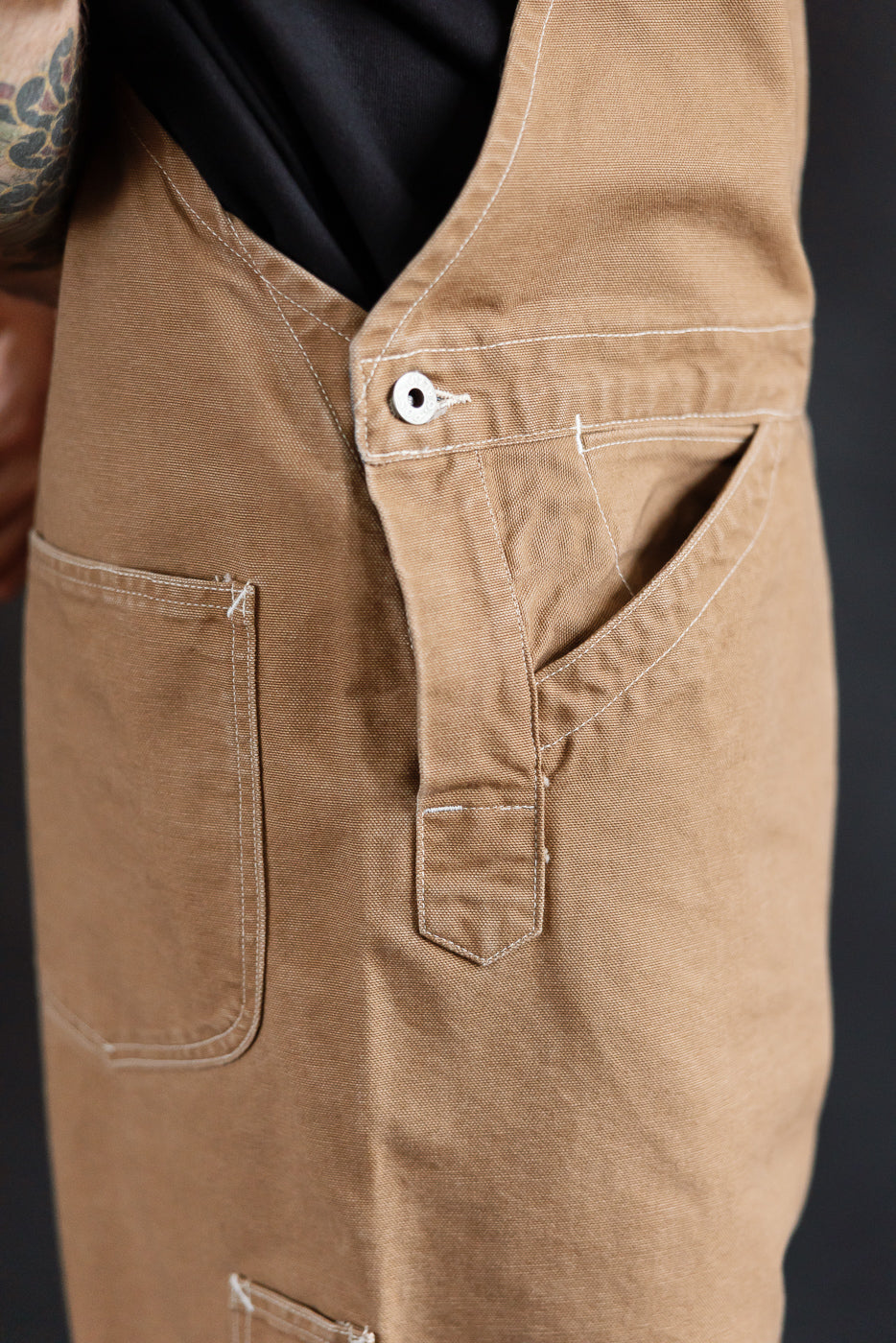 Close-up side view of Post O'Alls brown pigment dyed canvas overalls on male model, highlighting pocket, button, and fabric texture at Dant.