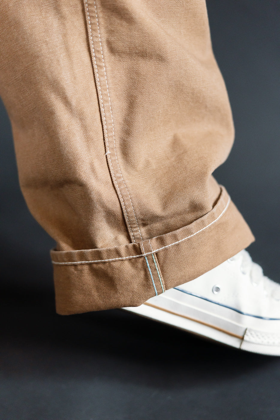Close-up of hem and stitching on POST 46 brown canvas overalls, left leg side, worn by male model, for Dant contemporary casual apparel.