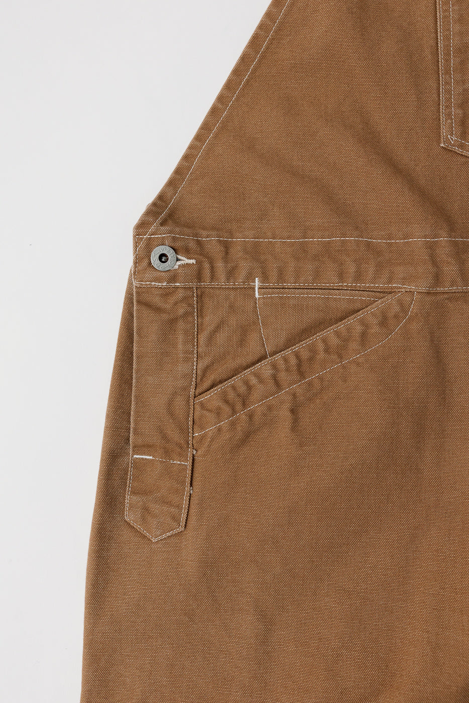 Close-up of front right side pocket and button detail on brown pigment-dyed canvas overalls