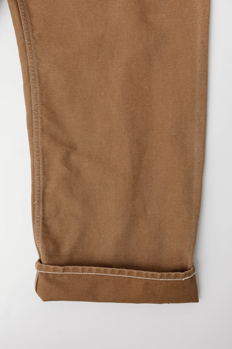 Close-up of front leg hem, brown pigment-dyed canvas overalls, showing cuff and stitching detail