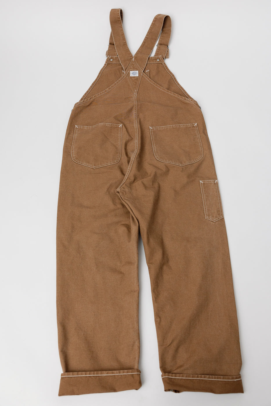 Flat lay of Post O’Alls pigment dyed brown canvas overalls, back view, showing rear pockets and workwear details.