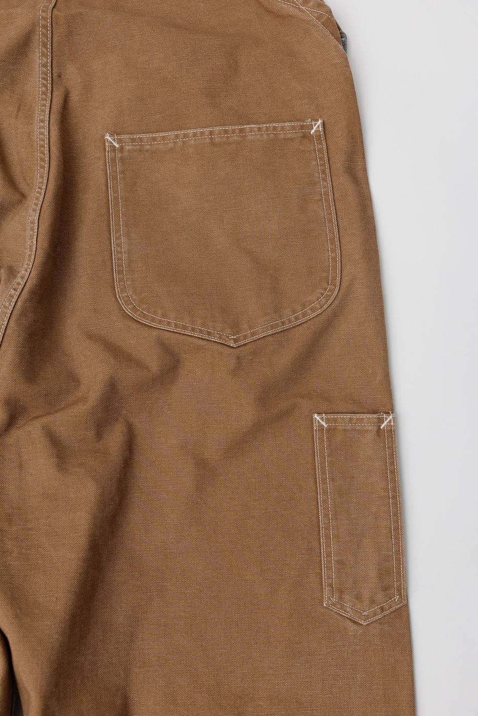 Close-up of back right side of pigment dyed brown canvas overalls showing two back pockets and contrast stitching, Dant contemporary casual apparel.