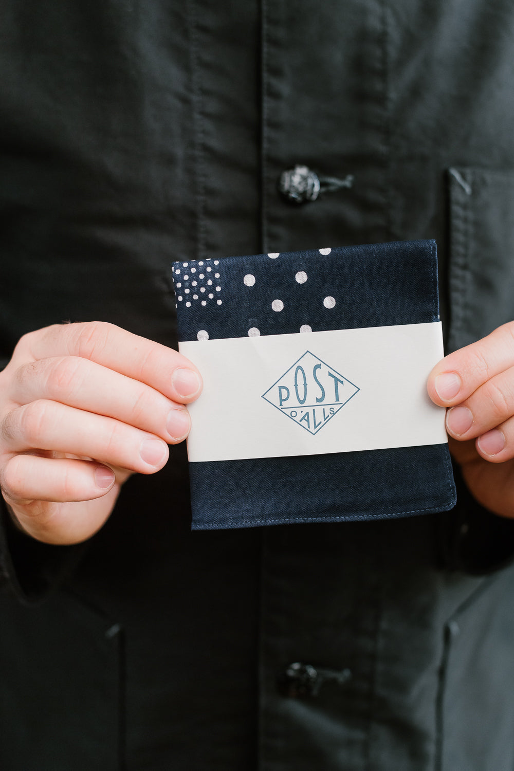Close-up of male model holding Post O'Alls navy bandana hankie, front view, polka dot detail