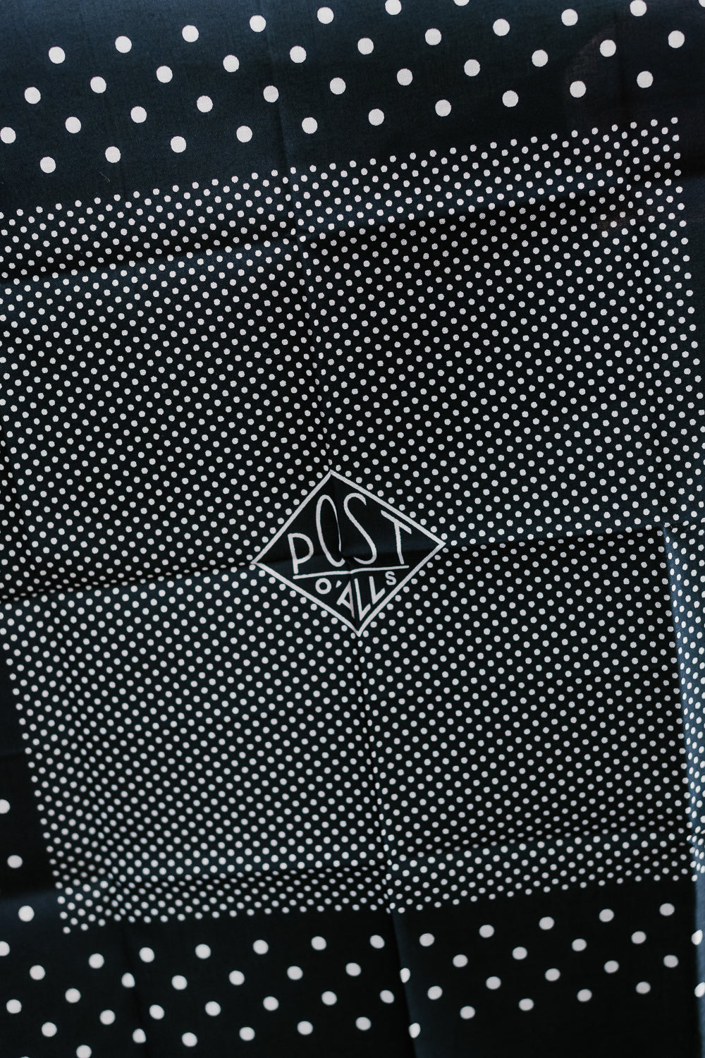 Close-up of Post O’alls navy bandana with polka dots and logo, front flat lay detail