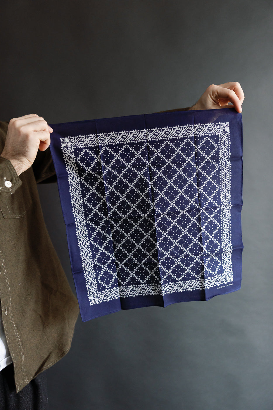 Close-up of navy bandana with white stitch design, front side, held by model's hands, Dant casual accessories