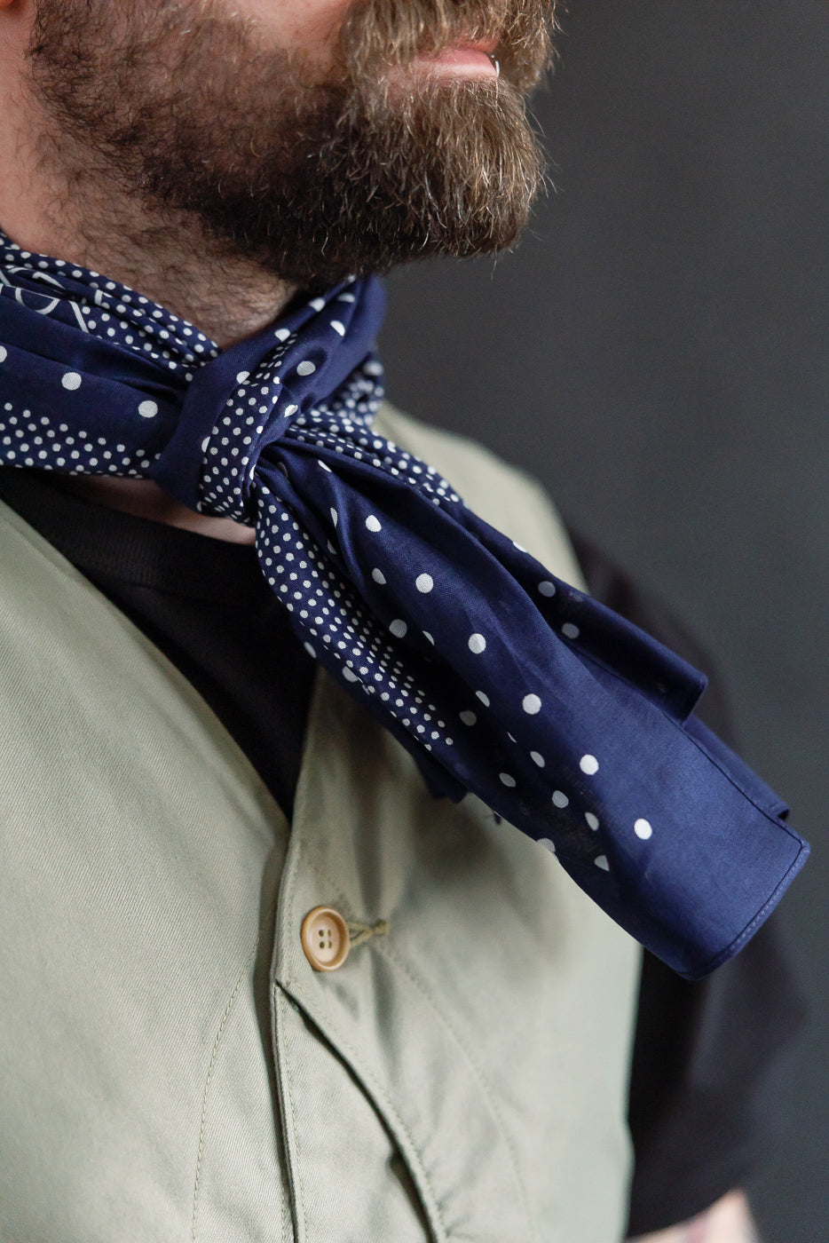 Close-up of navy bandana scarf with polka dot pattern tied at the neck on male model, chest view.