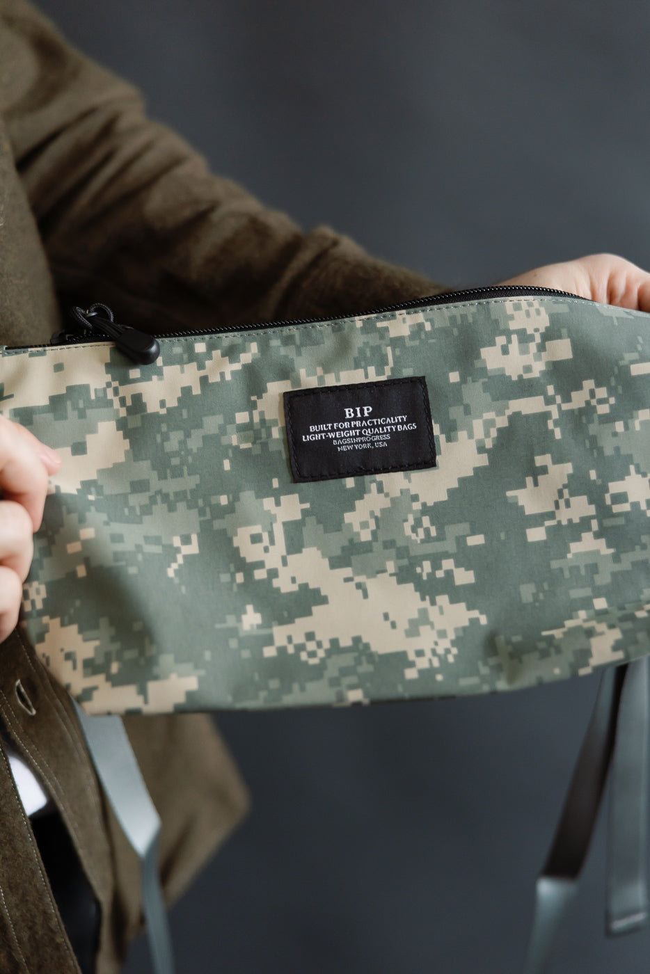 Close-up of male model holding digital camo desert fanny pack, front patch and zipper detail visible.
