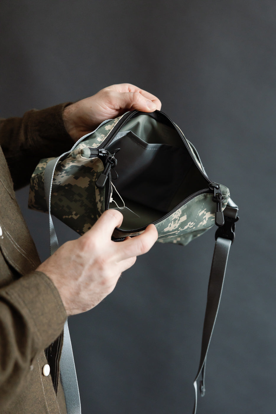 Close-up of digital camo crossbody fanny pack interior, male hand holding open top view