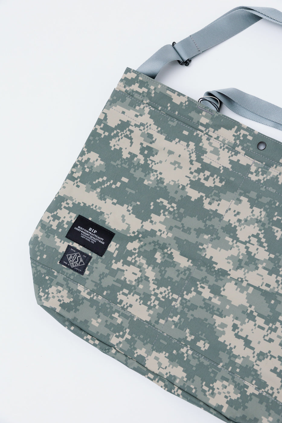 Close-up of Post O’Alls New York tote bag in desert digital camo Gore-Tex, flat lay front view, showing black logo tags and sturdy grey strap, contemporary accessory at Dant.