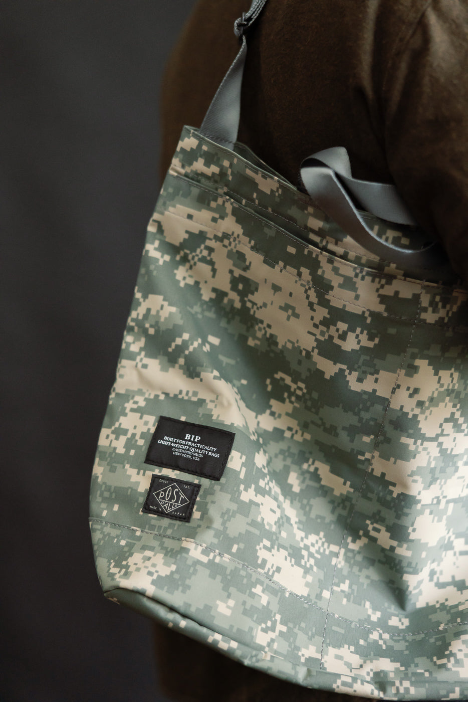 Close-up of digital camo desert tote bag with logo patches, shown on right side of male model, 5'9