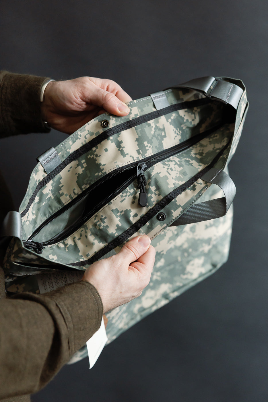 Close-up of male model holding Post O'Alls New York tote in desert digital camo, top zipper detail