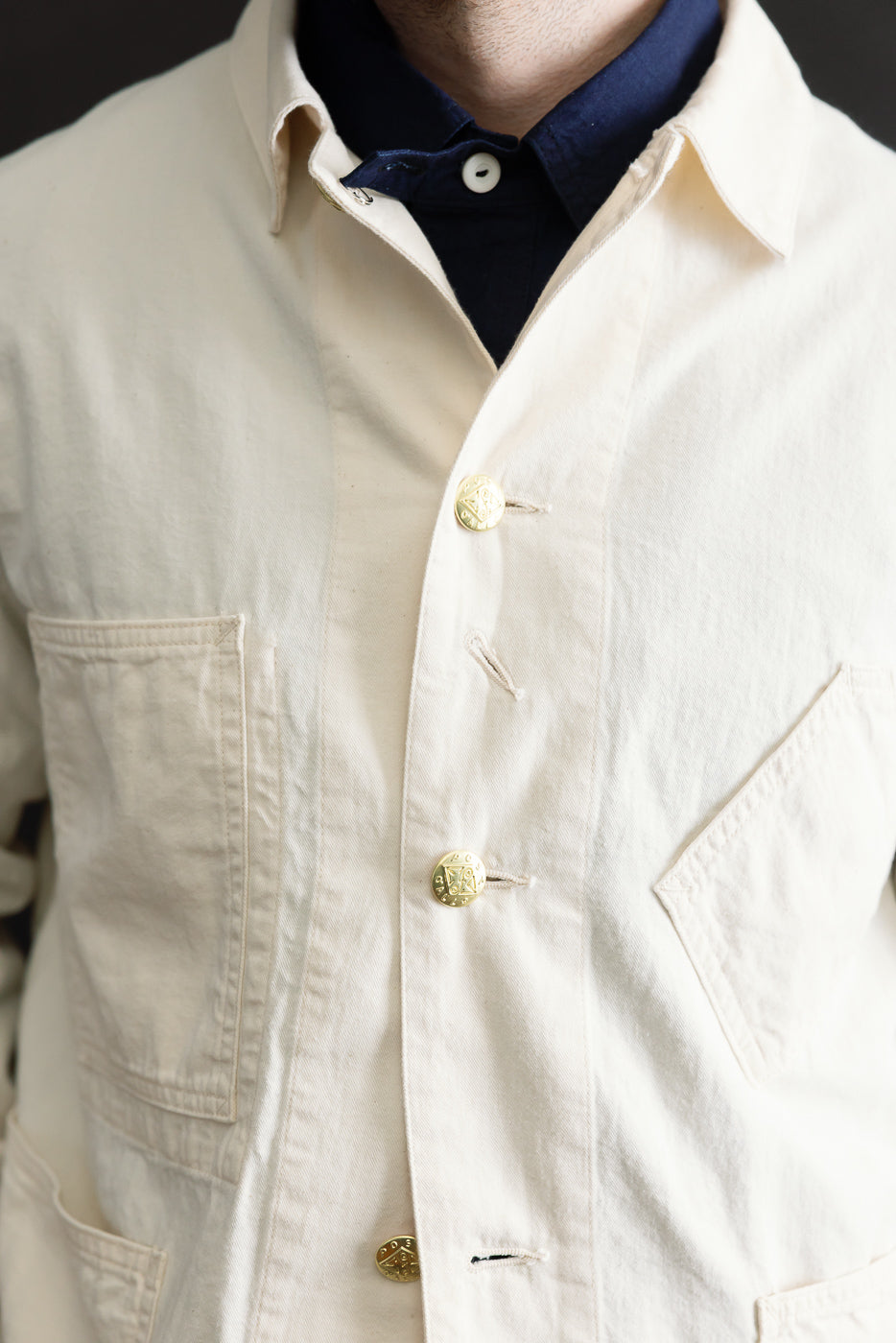 Close-up front view of mid-weight natural denim jacket on male model, 5'9, 165lbs, athletic build; highlights brass buttons, collar, textured fabric, and front pockets.