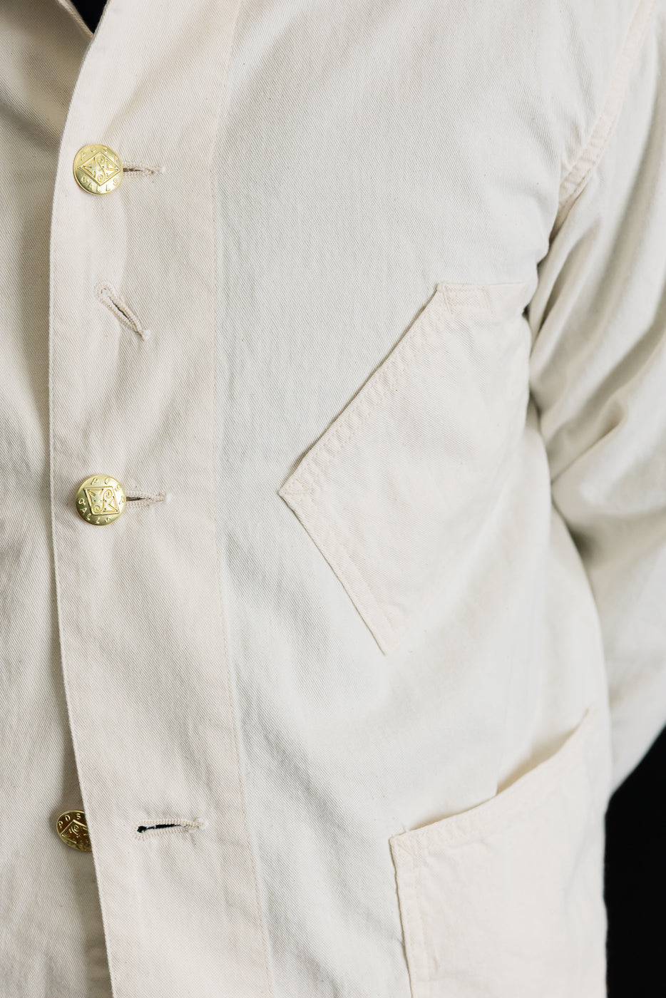 Close-up of mid-weight natural denim jacket front, showing metal buttons, angled chest pocket detail, and fabric texture on male model, 5'9