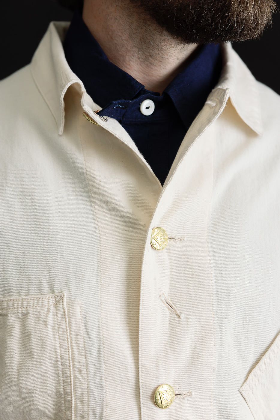 Close-up front of men's natural denim jacket, gold buttons, chest pocket; model is male, 5'9
