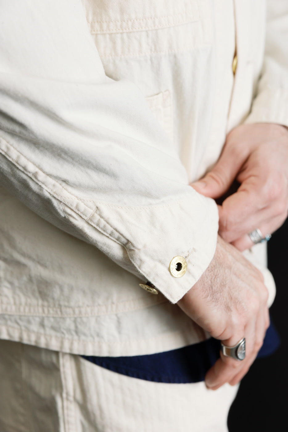 Close-up of a male model’s left arm showing the cuff and sleeve button detail of a natural mid-weight denim jacket, side view.