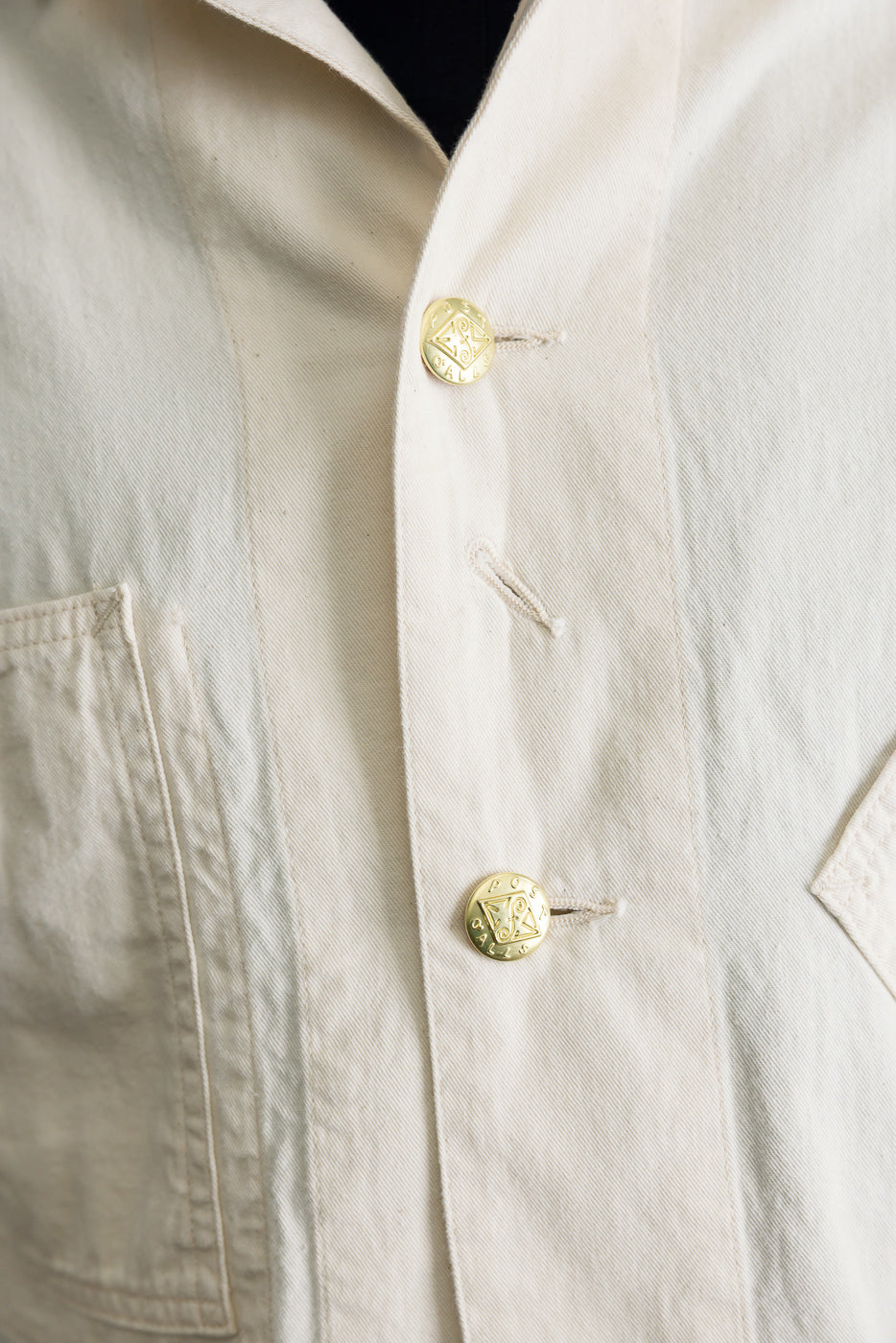 Close-up of front chest of natural mid-weight denim jacket, showing gold buttons and pocket detail.