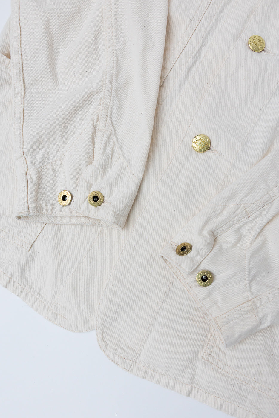Close-up of natural mid-weight denim jacket front hem and sleeve cuffs with brass snap buttons