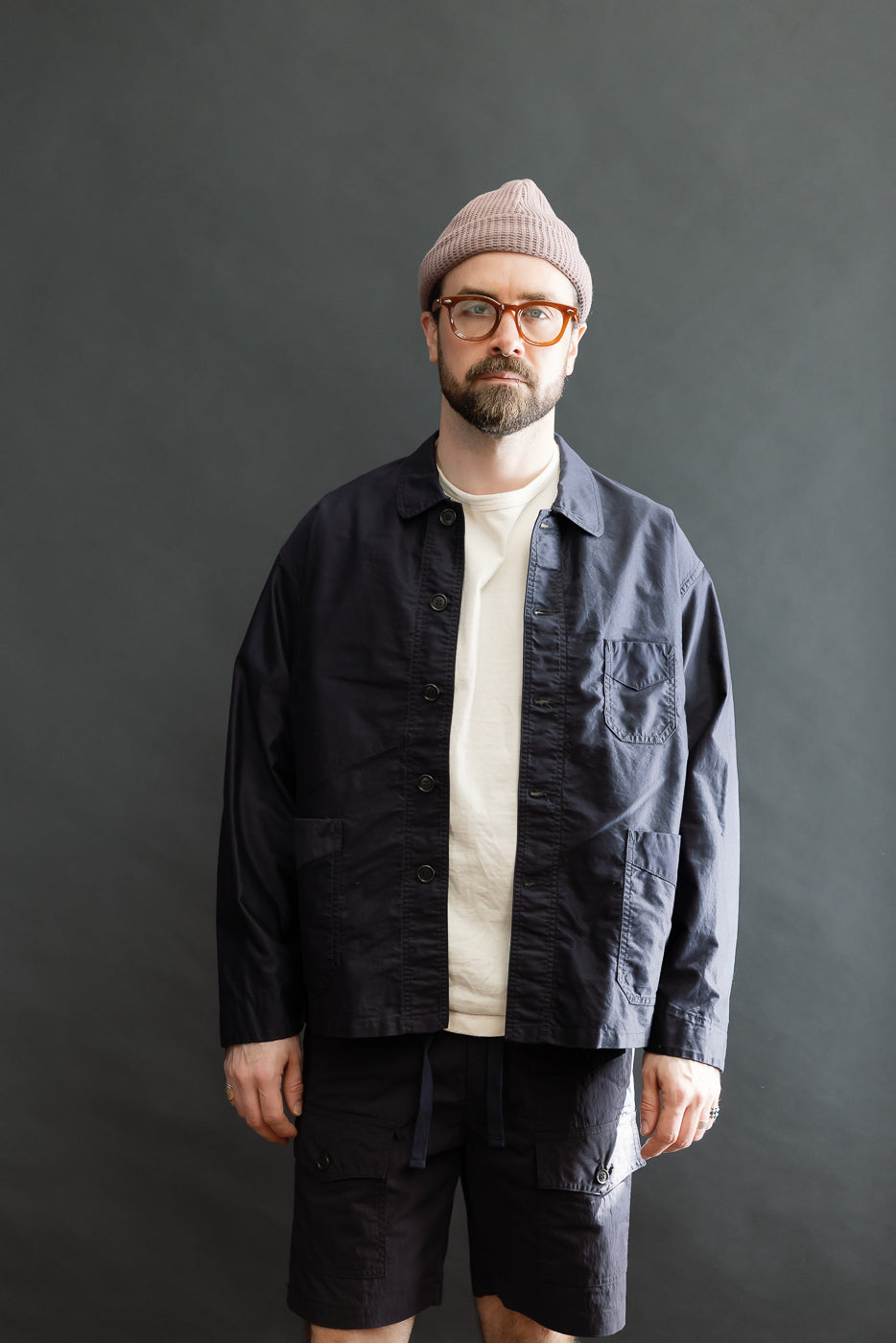 Man wearing 3135-LMN - Post Chinois Travail 2 Light Moleskin jacket in dark navy, showcasing its relaxed, cropped fit and rounded collar. Styled with cargo shorts, embodying Dant's premium workwear aesthetic.