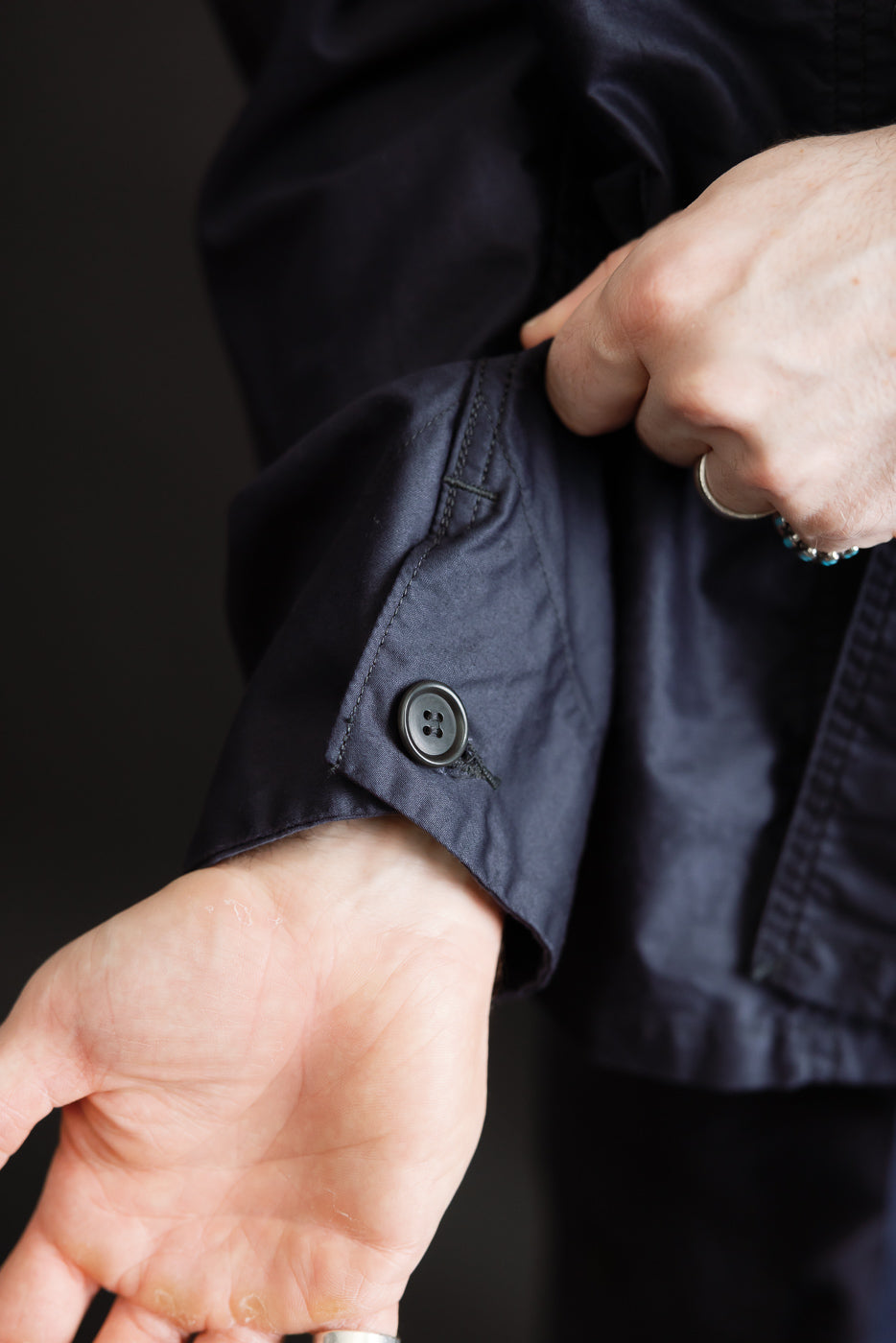 Close-up of a hand adjusting the cuff of the 3135-LMN Post Chinois Travail 2 Light Moleskin jacket in dark navy, showcasing its pre-washed cotton moleskin fabric and sleeve button detail.